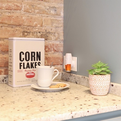 Lata de corn flakes, chávena com bolos, difusor de aroma e planta numa bancada de cozinha.