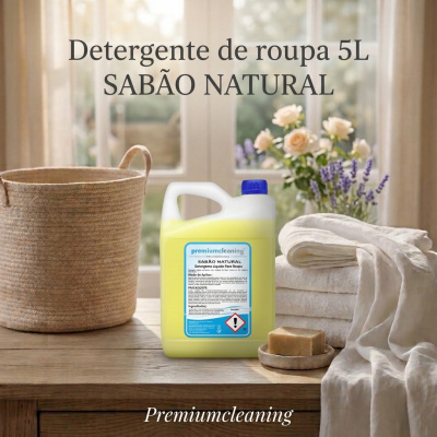 Detergente de roupa 5L amarelo em embalagem plástica com tampa azul, rodeado por toalhas brancas, cesta de fibra e flores sobre mesa de madeira