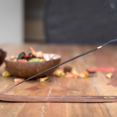 Incensório de madeira com incenso aceso emitindo fumo sobre mesa de madeira