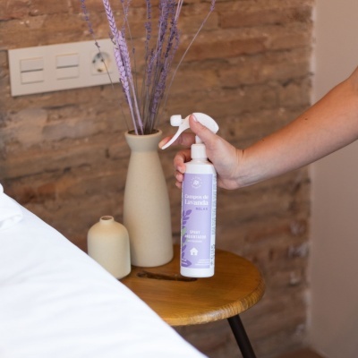 Frasco branco de spray ambientador lilás sobre mesa de madeira com vasos e flores secas