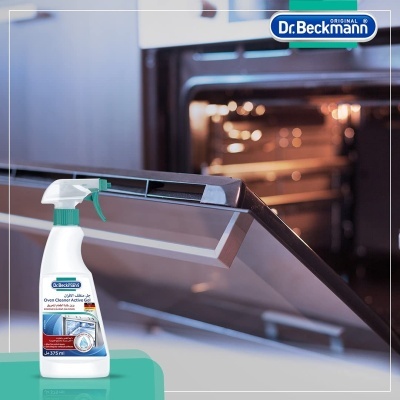 Spray de limpeza para forno Dr. Beckmann com gatilho verde sobre superfície verde e forno aberto ao fundo