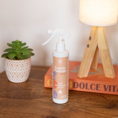 Spray ambientador canela naranja sobre mesa com livro e planta