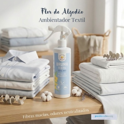 Frasco branco de bruma têxtil com roupas dobradas e algodão sobre mesa de madeira