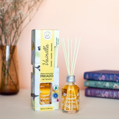 Difusor de aroma de baunilha com frasco de vidro e varetas ao lado de caixa com texto e design floral