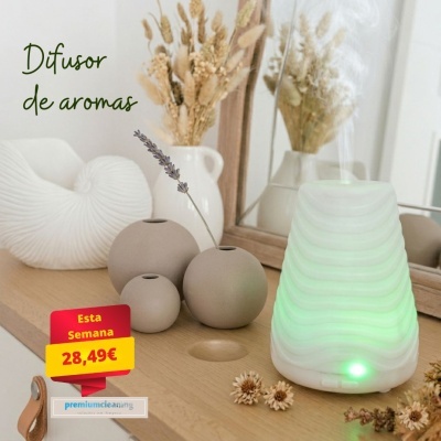 Difusor de aromas branco com luz verde sobre móvel de madeira com vasos redondos cinza e jarra branca com flores secas