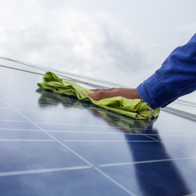 Mão com camisola azul limpa painel solar azul com pano verde claro sob céu nublado