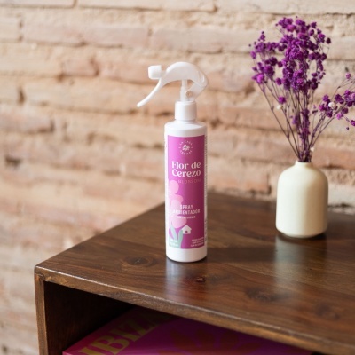 Spray ambientador Flor de Cerezo Blossom sobre móvel de madeira com jarro branco e flores secas roxas