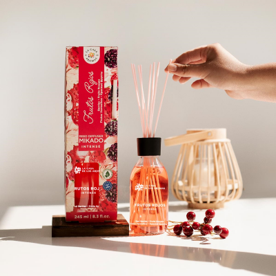 Difusor mikado com líquido rosa claro e embalagem vermelha com texto e detalhes florais