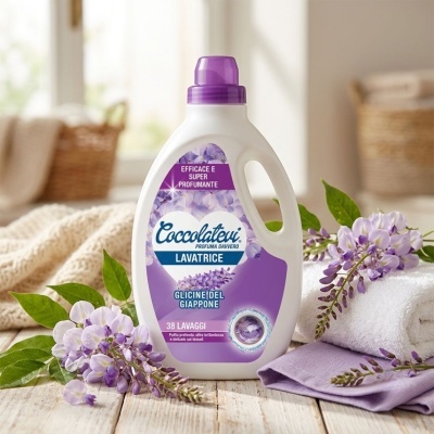 Produto líquido Coccolateu Lavatrice com flores roxas, toalha branca e pano roxo sobre superfície de madeira.