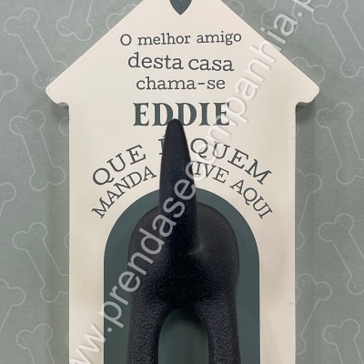Objeto decorativo de parede em forma de casa com gancho em rabo de cão preto e texto em português.