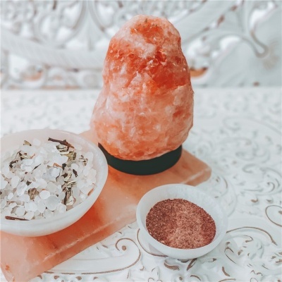 Lâmpada de sal rosa com dois recipientes pequenos, um com sal grosso e ervas e outro com pó castanho
