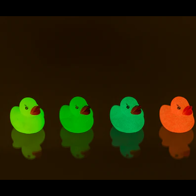 Quatro patinhos de borracha fluorescentes em várias cores sobre superfície escura.