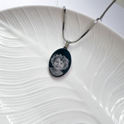 Colar com pendente oval preto com gravura de rosto de criança sobre fundo branco texturizado