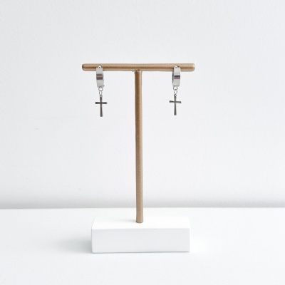 Par de argolas prateadas com cruz pendente em exposição num suporte dourado