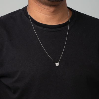 Colar masculino prateado com pendente redondo pequeno sobre t-shirt preta.