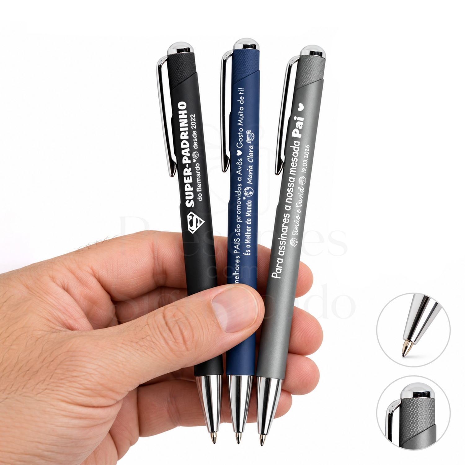 Caneta Personalizada de Toque Suave com Detalhes Prateados Três esferográficas mate preto, azul e cinza com texto branco e clip metálico seguradas por mão