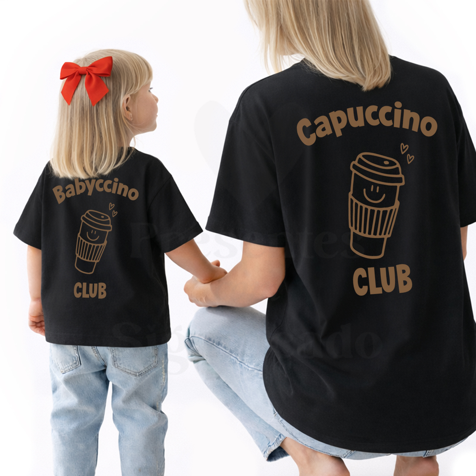 Conjunto Mãe e Filho(a) Personalizado - Capuccino Club / Babyccino Club Duas t-shirts pretas com estampas de copos de café e texto, adulto e criança de costas, criança com laço vermelho no cabelo e jeans claros