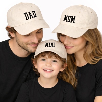 Três pessoas com bonés bege e t-shirts pretas com textos DAD, MOM e MINI