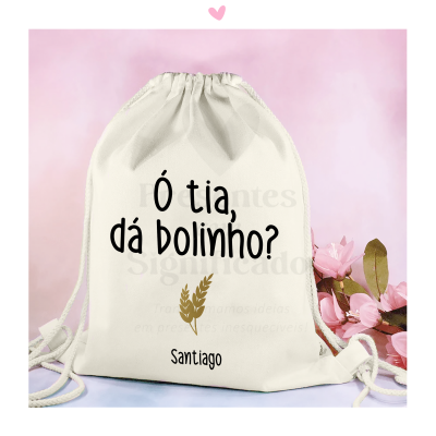 Mochila branca de tecido com cordões e texto preto 'Ó tia, dá bolinho?', nome 'Santiago' e imagem dourada de espigas de trigo.