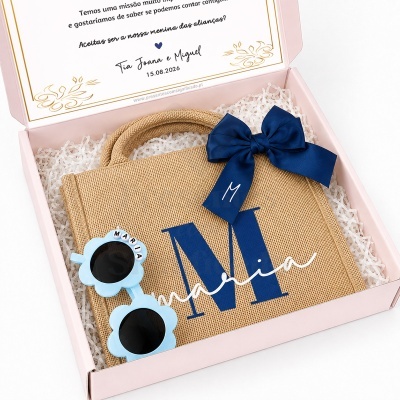 Caixa rosa com mala de palha personalizada e óculos de sol azuis.