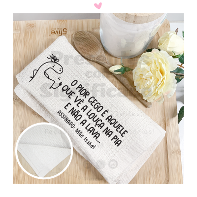 Toalha de cozinha branca com texto em preto e desenho, ao lado colher de pau e flores brancas em vaso