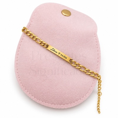 Pulseira dourada com placa gravada sobre bolsa rosa de veludo