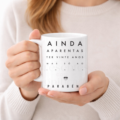 Caneca branca com texto em preto estilo tabela de visão, segurada por mão com camisola creme.
