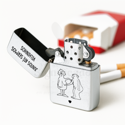 Isqueiro metálico prateado com ilustração e texto, com caixa de cigarros ao fundo
