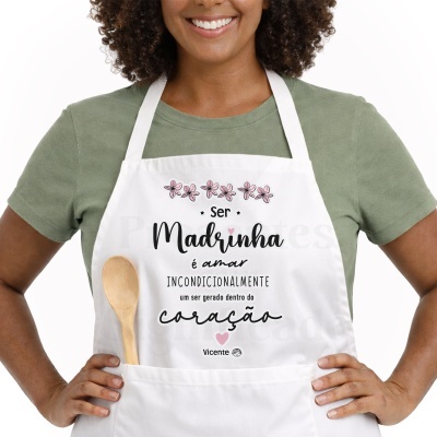 Avental branco com texto e flores usado por pessoa com camisola verde e colher de madeira no bolso
