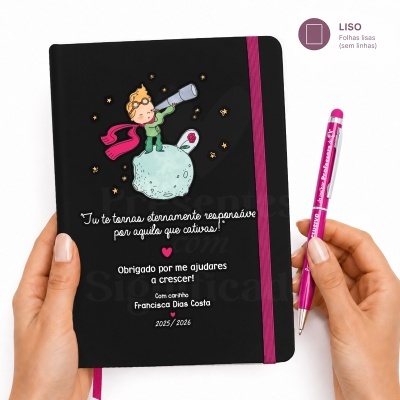 Caderno preto com elástico rosa, ilustração de criança e texto em branco, segurado por mãos, com caneta rosa ao lado