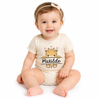 Bebé de body bege com girafa e texto Matilde, fita de cabelo bege com laço