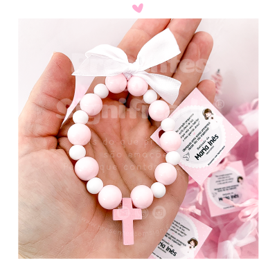 Pulseira elástica rosa e branca com cruz e laço branco num mão