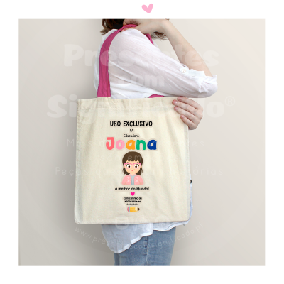 Sacola de tecido com estampa colorida e texto em português, sendo usada por mulher com camisa branca e calças jeans.