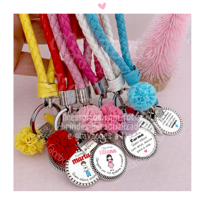 Porta-chaves coloridos em couro trançado com medalhões personalizados e pompons sobre fundo rosa.