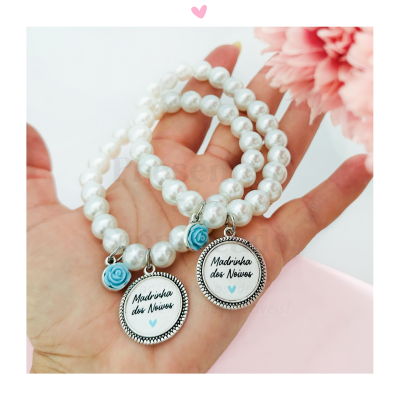Pulseiras de pérolas brancas com pendentes e detalhes azuis, seguradas na mão