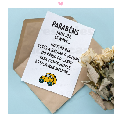 Cartão comemorativo branco com texto humorístico e desenho de carro amarelo, envelope castanho e flores secas ao lado