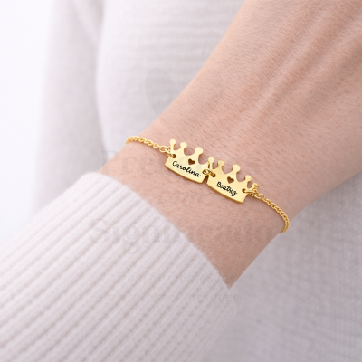Pulseira dourada com pendentes em forma de coroa com nomes Carolina e Beatriz no pulso