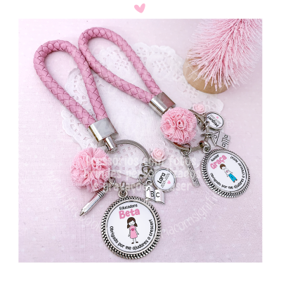 Dois porta-chaves rosa com cordões trançados e medalhões com desenhos e nomes