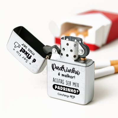 Isqueiro metálico prateado aberto com texto personalizado junto de caixa de cigarros e cigarros no fundo