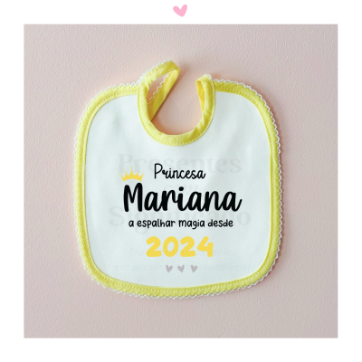 Babete branco com borda amarela e texto impresso, sobre fundo rosa claro.