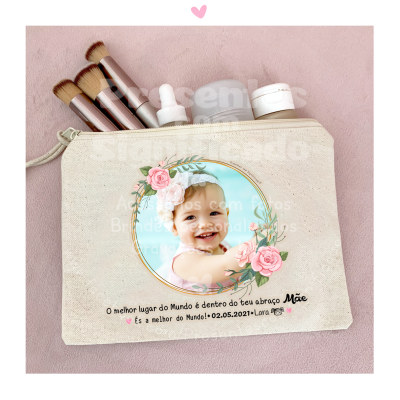 Necessaire bege com foto de bebé e texto em português, rodeada por pinceis e frascos de cosméticos