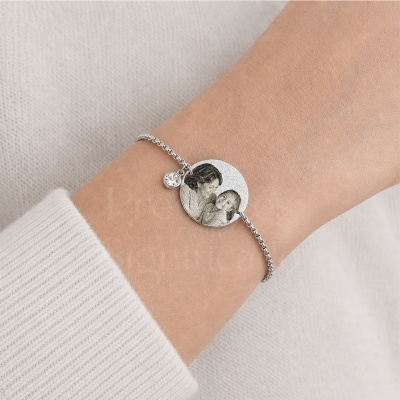 Pulseira prateada com pendente redondo gravado usada no pulso