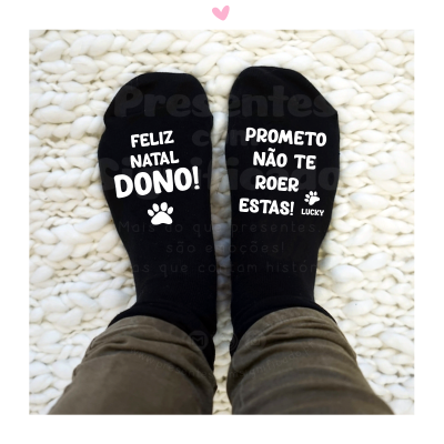 Meias pretas com texto de Natal e promessa para dono, sobre tapete branco.