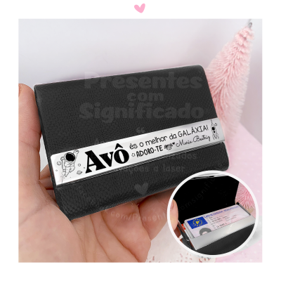 Carteira preta com barra metálica com texto a segurada na mão com decoração cor de rosa ao fundo.