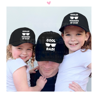 Duas crianças e um adulto com bonés pretos e t-shirts brancas, bonés com frases em branco relacionadas ao pai.