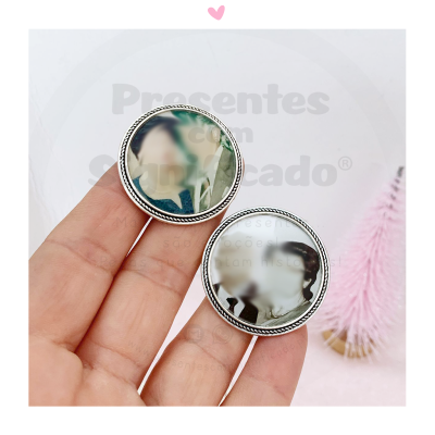 Botões redondos com fotos personalizadas e borda prateada, segurados em mão, fundo com objeto rosa