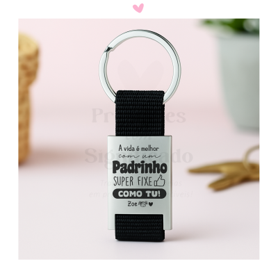 Porta-chaves prateado com fita preta e gravação preta com texto em português para padrinho, em fundo rosa.