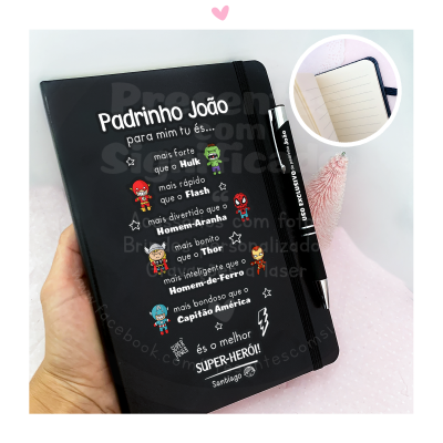 Caderno preto personalizado com texto em português e desenhos de super-heróis, com caneta preta, numa mão