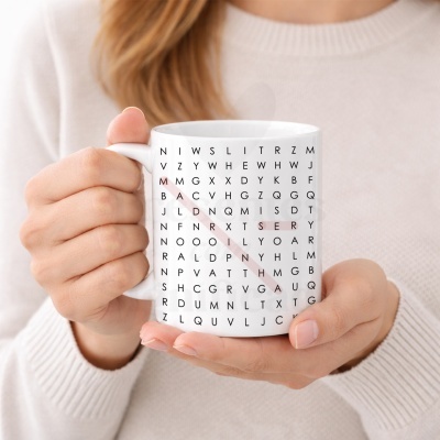 Caneca branca com padrão de letras negras em grelha tipo sopa de letras, detalhes em vermelho, segura por mãos femininas