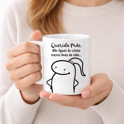 Caneca branca com mensagem para mãe e desenho simples, segurada por mulher com camisola bege